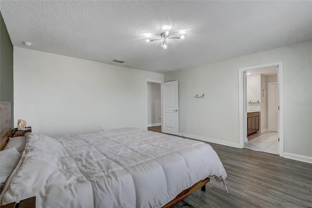 bedroom with ensuite bathroom, light hardwood / wood-style floors, and a textured ceiling