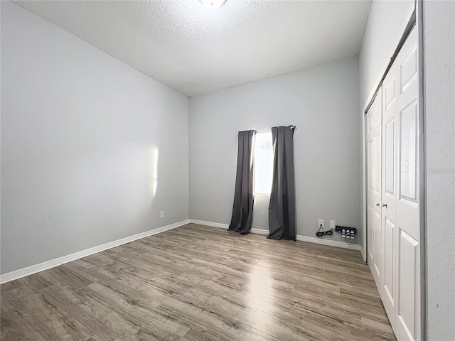 unfurnished bedroom with a closet, light hardwood / wood-style floors, multiple windows, and a textured ceiling