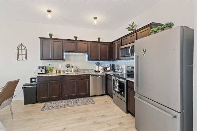 kitchen with dark brown cabinetry, sink, appliances with stainless steel finishes, light hardwood / wood-style floors, and backsplash