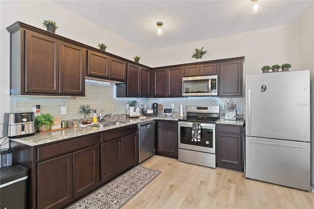 kitchen with sink, light hardwood / wood-style flooring, appliances with stainless steel finishes, dark brown cabinetry, and light stone countertops