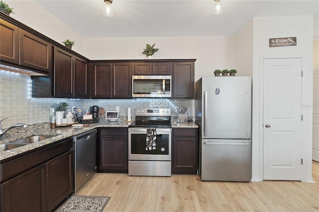 kitchen with stainless steel appliances, light stone countertops, sink, and light wood-type flooring