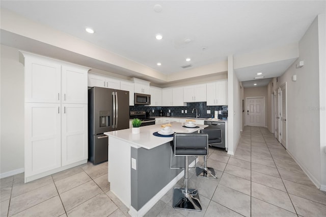 kitchen featuring appliances with stainless steel finishes, a breakfast bar, tasteful backsplash, white cabinets, and a center island