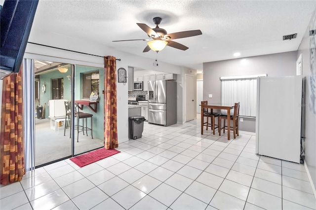 kitchen with light tile patterned flooring, appliances with stainless steel finishes, tasteful backsplash, white cabinets, and ceiling fan