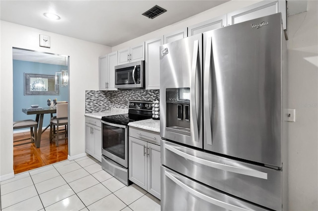 kitchen with backsplash, light tile patterned floors, stainless steel appliances, and light stone countertops