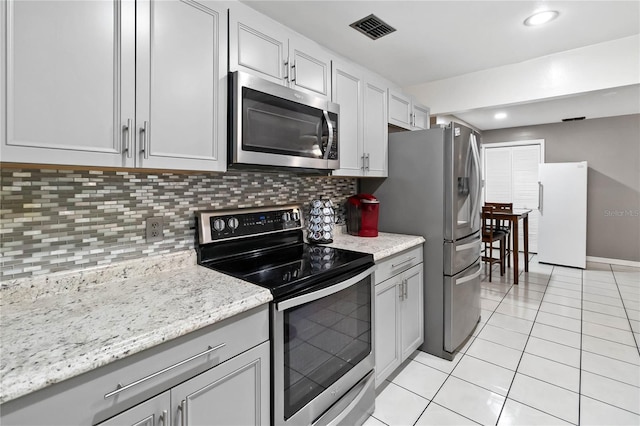 kitchen featuring tasteful backsplash, light tile patterned flooring, appliances with stainless steel finishes, and light stone counters