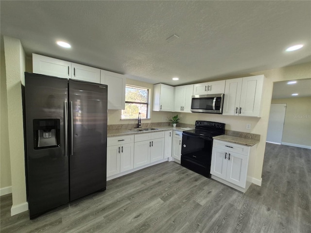 kitchen with sink, a textured ceiling, light wood-type flooring, appliances with stainless steel finishes, and white cabinets