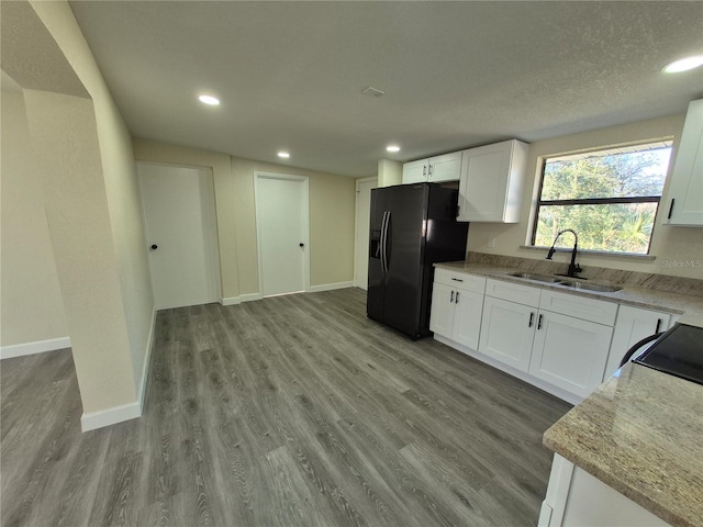 kitchen with sink, light stone counters, white cabinets, black fridge, and light wood-type flooring