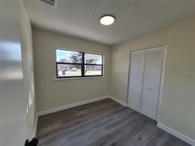 unfurnished bedroom with dark hardwood / wood-style floors, a textured ceiling, and a closet