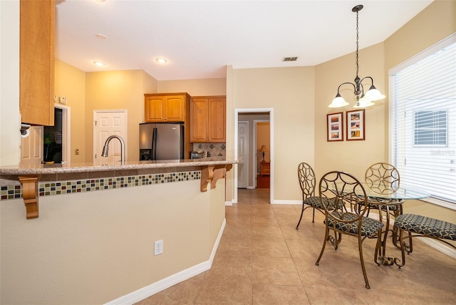 kitchen featuring sink, stainless steel fridge, hanging light fixtures, a kitchen bar, and light tile patterned flooring