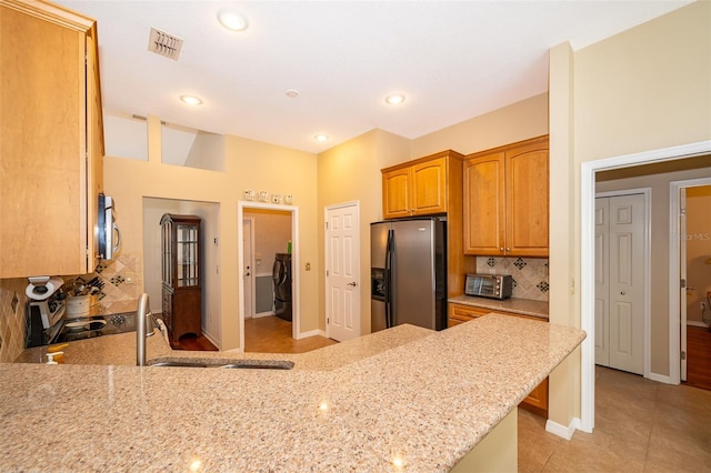 kitchen featuring washing machine and dryer, light stone countertops, appliances with stainless steel finishes, and kitchen peninsula