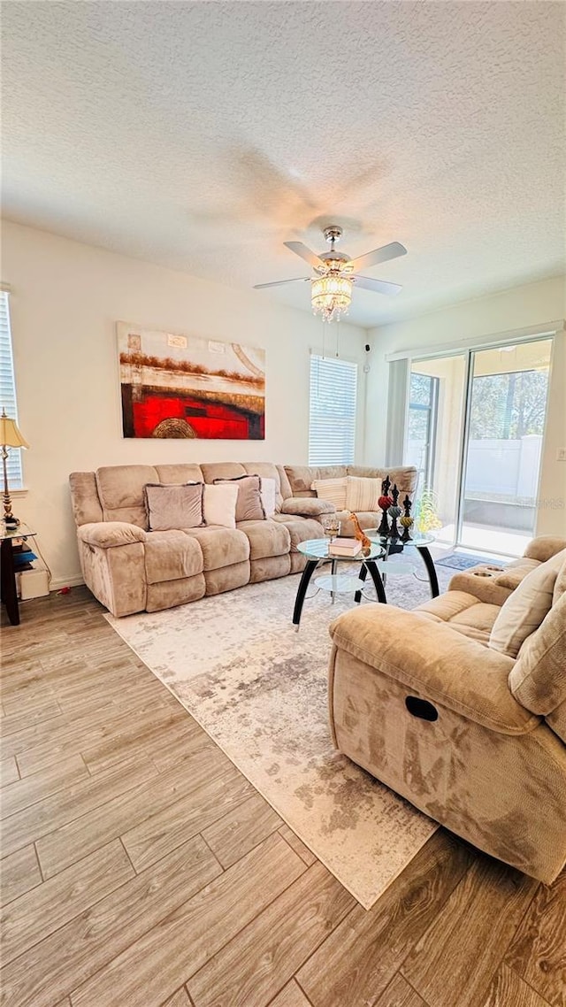 living room with ceiling fan, a textured ceiling, and light wood-type flooring