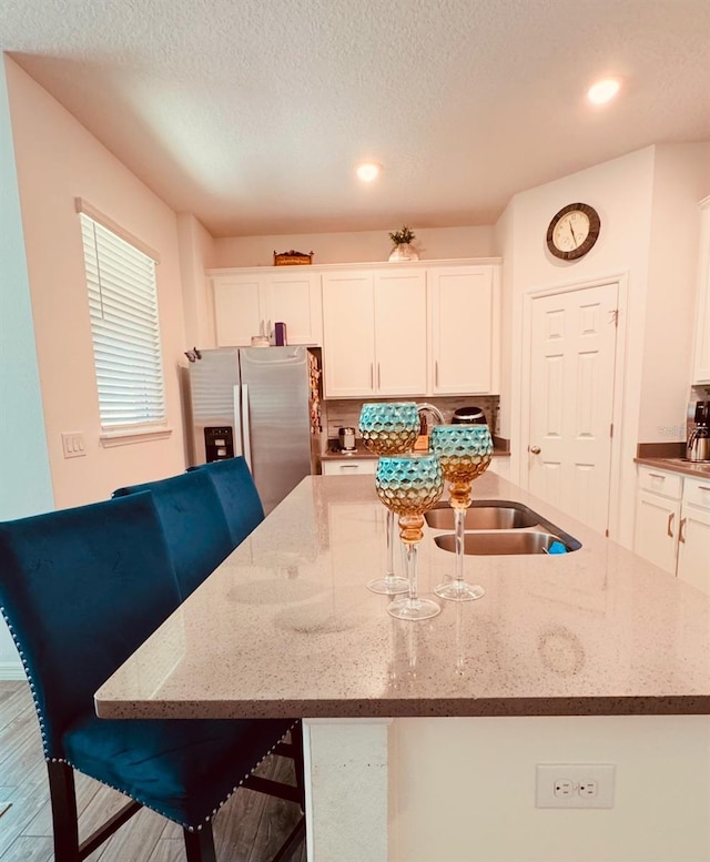 kitchen featuring a breakfast bar area, stainless steel refrigerator with ice dispenser, light stone countertops, an island with sink, and white cabinets