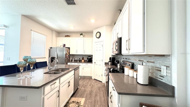 kitchen with sink, a kitchen island with sink, stainless steel appliances, white cabinets, and light wood-type flooring