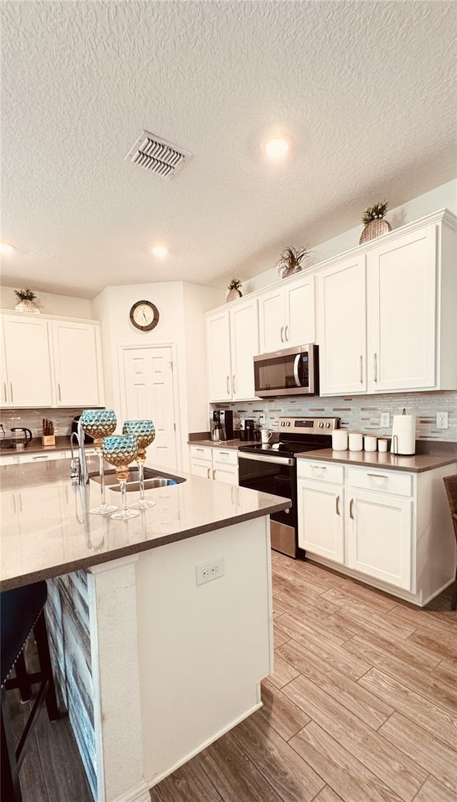 kitchen featuring white cabinetry, appliances with stainless steel finishes, decorative backsplash, and light wood-type flooring