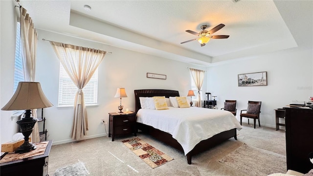 bedroom featuring light colored carpet, a textured ceiling, and a tray ceiling