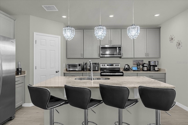 kitchen with a kitchen island with sink, hanging light fixtures, stainless steel appliances, and gray cabinetry