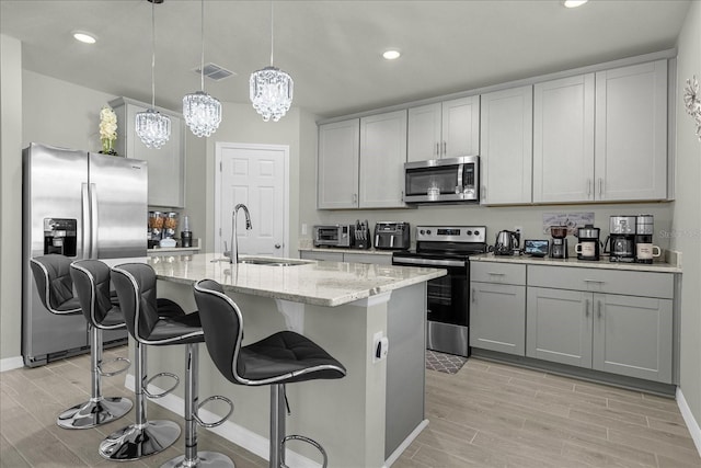 kitchen featuring sink, light stone counters, hanging light fixtures, a center island with sink, and appliances with stainless steel finishes