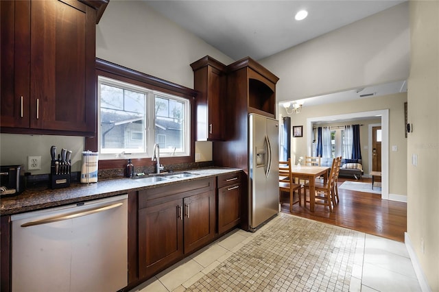 kitchen featuring stainless steel appliances, dark stone counters, a sink, and light tile patterned floors