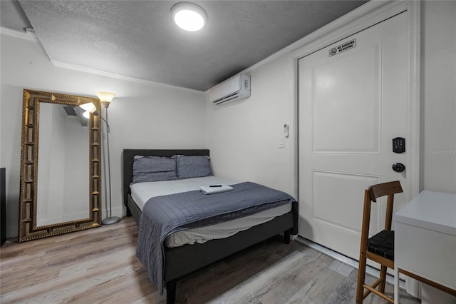 bedroom featuring light wood-style flooring, a textured ceiling, and a wall mounted AC