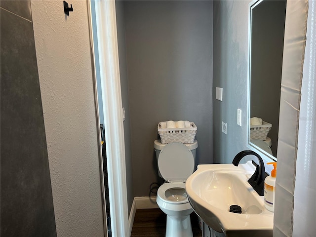 bathroom with a textured wall, toilet, a sink, wood finished floors, and baseboards