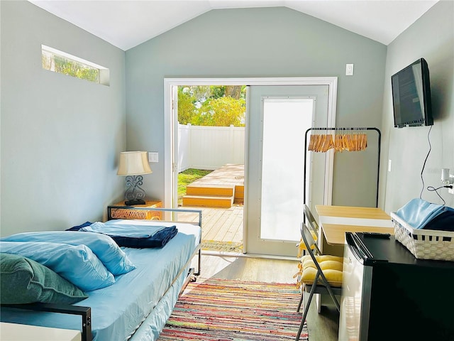 bedroom with lofted ceiling, multiple windows, wood finished floors, and freestanding refrigerator