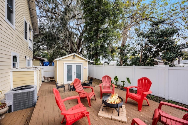 deck featuring a fire pit, a fenced backyard, an outbuilding, and cooling unit