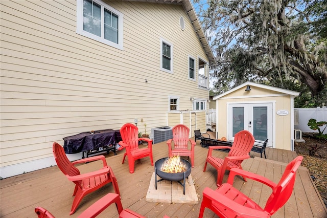 deck with a fire pit, central AC unit, an outbuilding, and fence