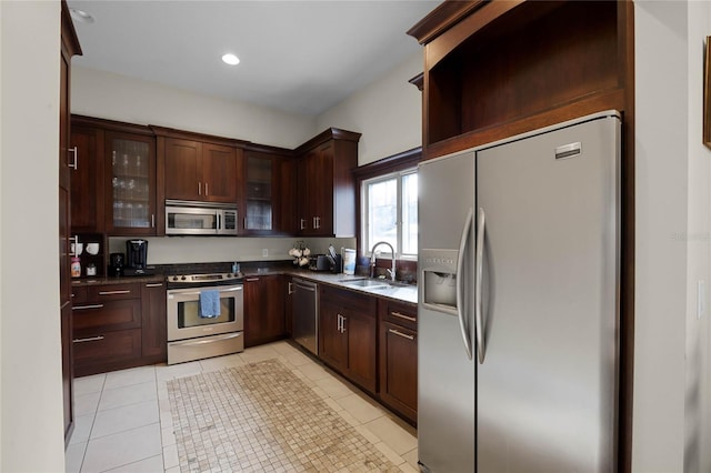 kitchen featuring light tile patterned floors, dark countertops, glass insert cabinets, stainless steel appliances, and a sink