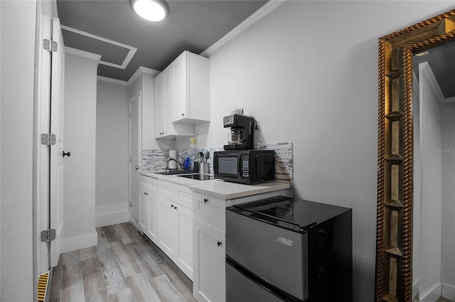 kitchen featuring black microwave, white cabinets, light wood-type flooring, freestanding refrigerator, and crown molding