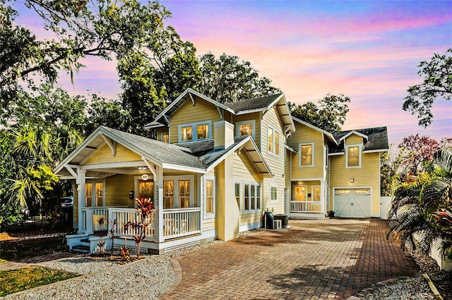 view of front facade featuring a garage, covered porch, central AC, and decorative driveway