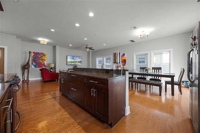 kitchen featuring visible vents, light wood-style floors, open floor plan, freestanding refrigerator, and dark stone countertops