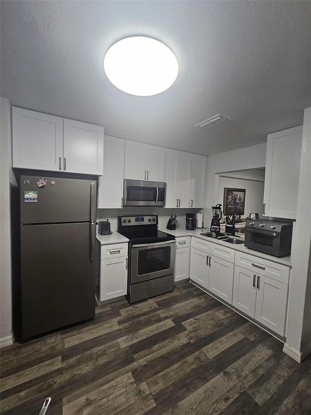 kitchen with appliances with stainless steel finishes, white cabinetry, sink, dark hardwood / wood-style flooring, and a textured ceiling