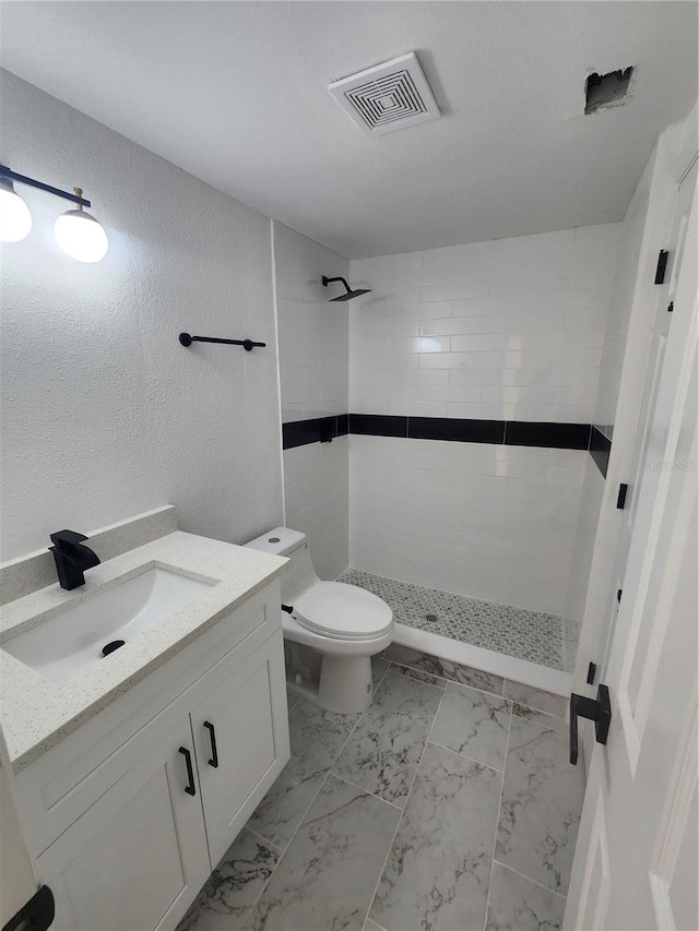 bathroom with tiled shower, vanity, and toilet