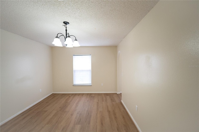 empty room featuring light wood-type flooring, a textured ceiling, and a chandelier