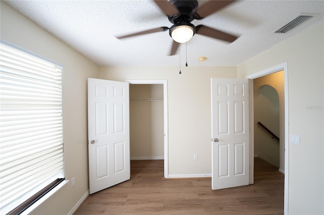 unfurnished bedroom featuring multiple windows, a walk in closet, a textured ceiling, and light wood-type flooring