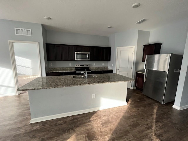 kitchen featuring light stone counters, sink, stainless steel appliances, and a center island with sink