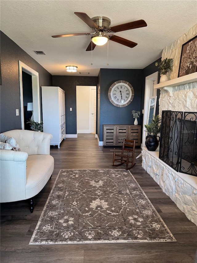 living room featuring ceiling fan, a fireplace, dark hardwood / wood-style flooring, and a textured ceiling