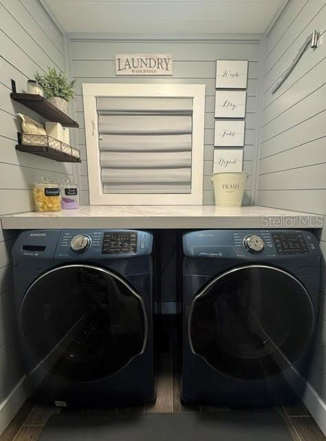 clothes washing area featuring wooden walls, dark hardwood / wood-style floors, and washing machine and clothes dryer