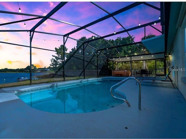 pool at dusk featuring a water view, a jacuzzi, a patio area, and a lanai