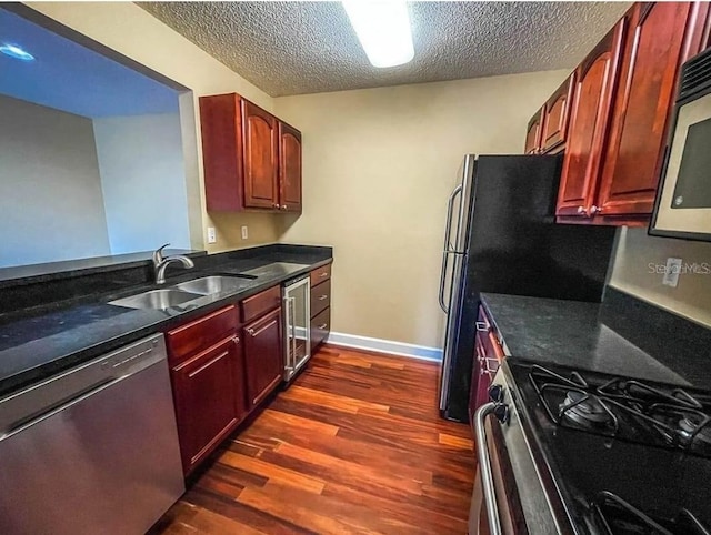 kitchen with appliances with stainless steel finishes, sink, beverage cooler, dark hardwood / wood-style flooring, and a textured ceiling