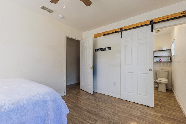 bedroom featuring hardwood / wood-style floors, a barn door, and ceiling fan