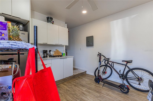 interior space featuring ceiling fan, electric panel, light hardwood / wood-style floors, and white cabinets