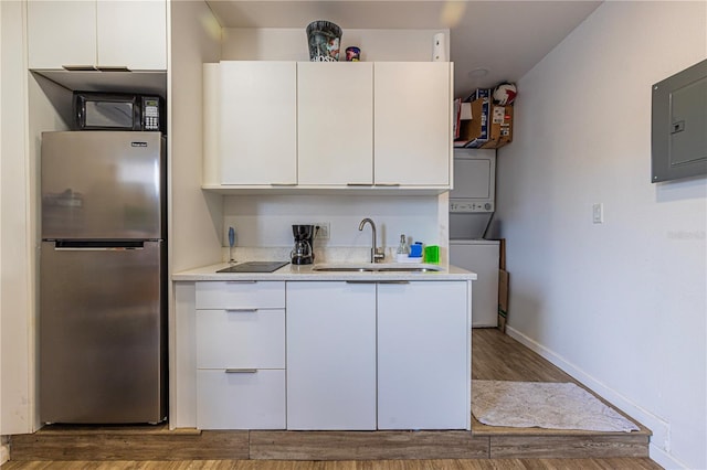 kitchen featuring white cabinetry, stacked washing maching and dryer, sink, and black appliances