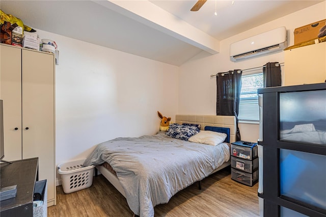 bedroom with ceiling fan, a wall mounted air conditioner, lofted ceiling with beams, and light hardwood / wood-style flooring