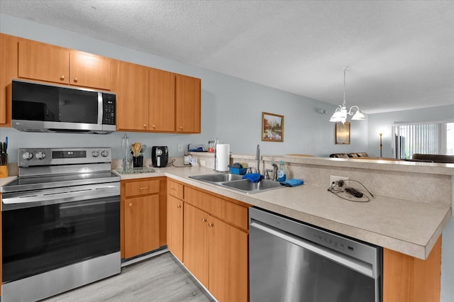 kitchen featuring appliances with stainless steel finishes, sink, light hardwood / wood-style floors, kitchen peninsula, and a textured ceiling