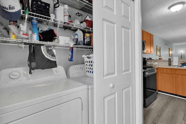 clothes washing area with light wood-type flooring, a textured ceiling, and washer and clothes dryer