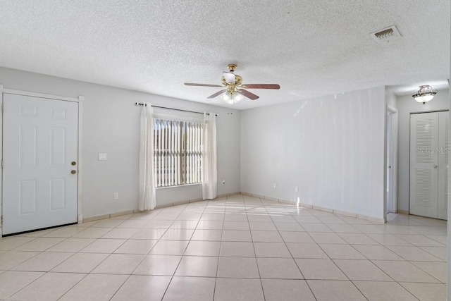 spare room with light tile patterned floors, a ceiling fan, visible vents, and a textured ceiling