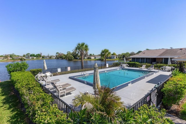 community pool with a patio, fence, and a water view