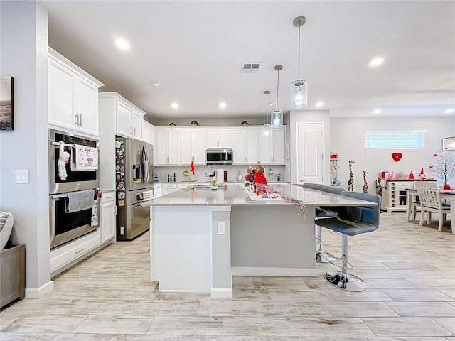 kitchen featuring a breakfast bar, white cabinetry, hanging light fixtures, a center island with sink, and stainless steel appliances