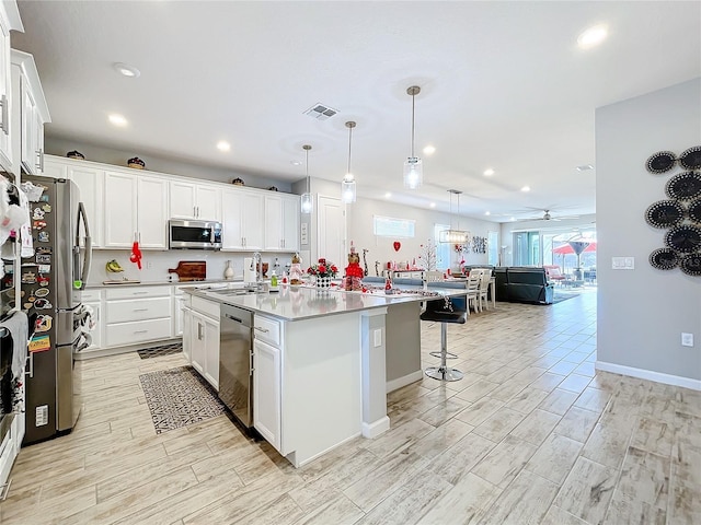 kitchen featuring sink, appliances with stainless steel finishes, an island with sink, white cabinets, and decorative light fixtures